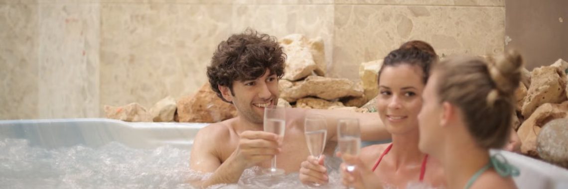 Group of friends toasting with drinks in a hot tub, enjoying relaxation and togetherness indoors.